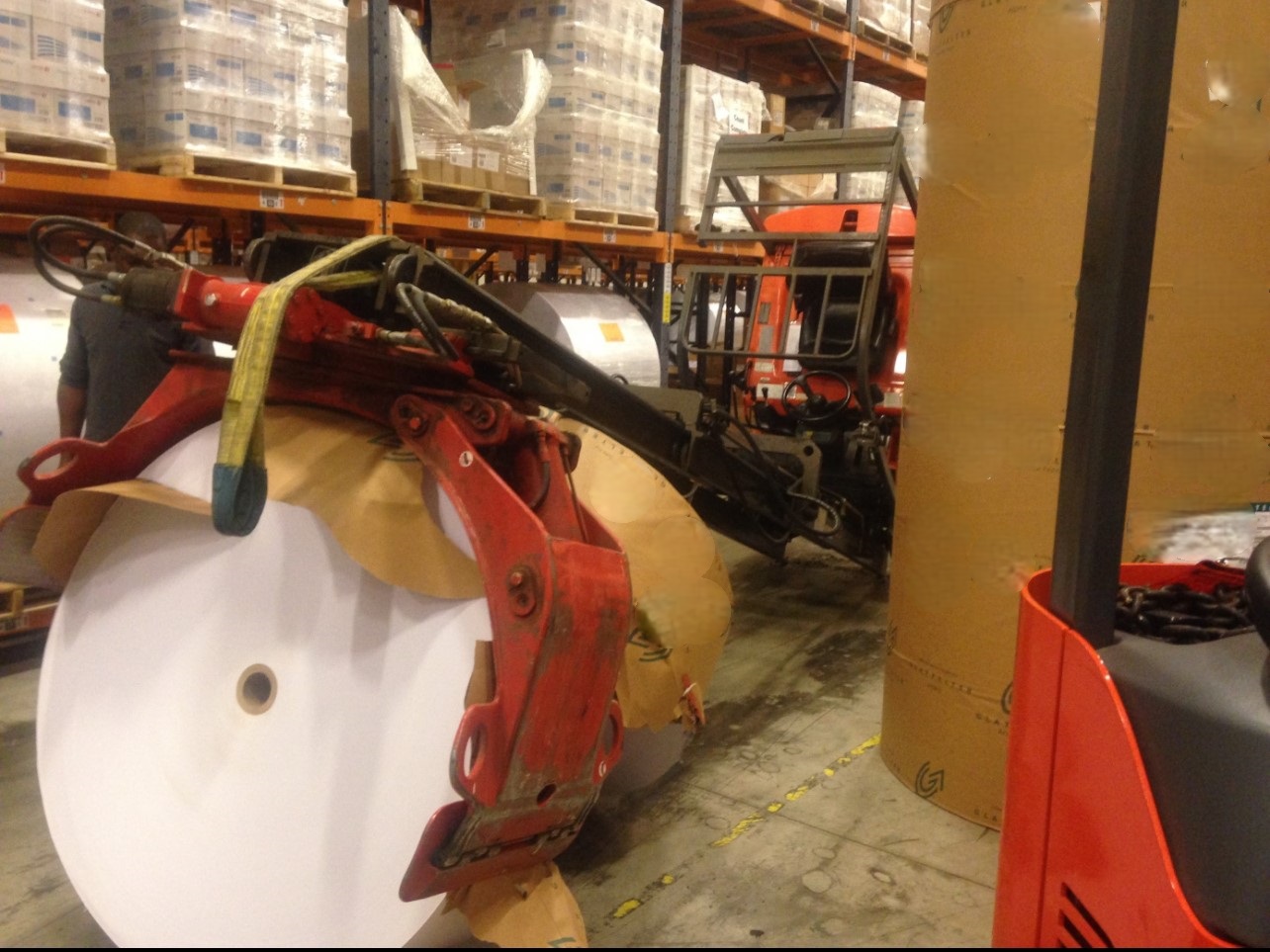 Lift truck with paper roll clamp attachment handling a large roll in a warehouse