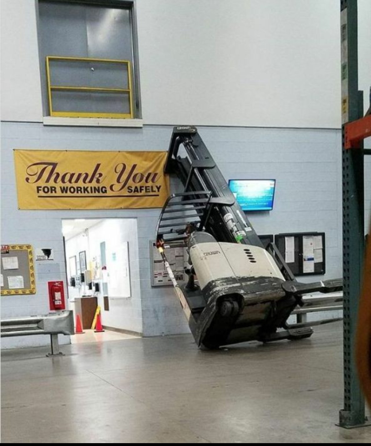 Stand-up reach truck tipped against a wall under a safety banner